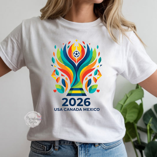 White t-shirt with colorful 2026 World Cup logo worn by a person, with a plant in the background.